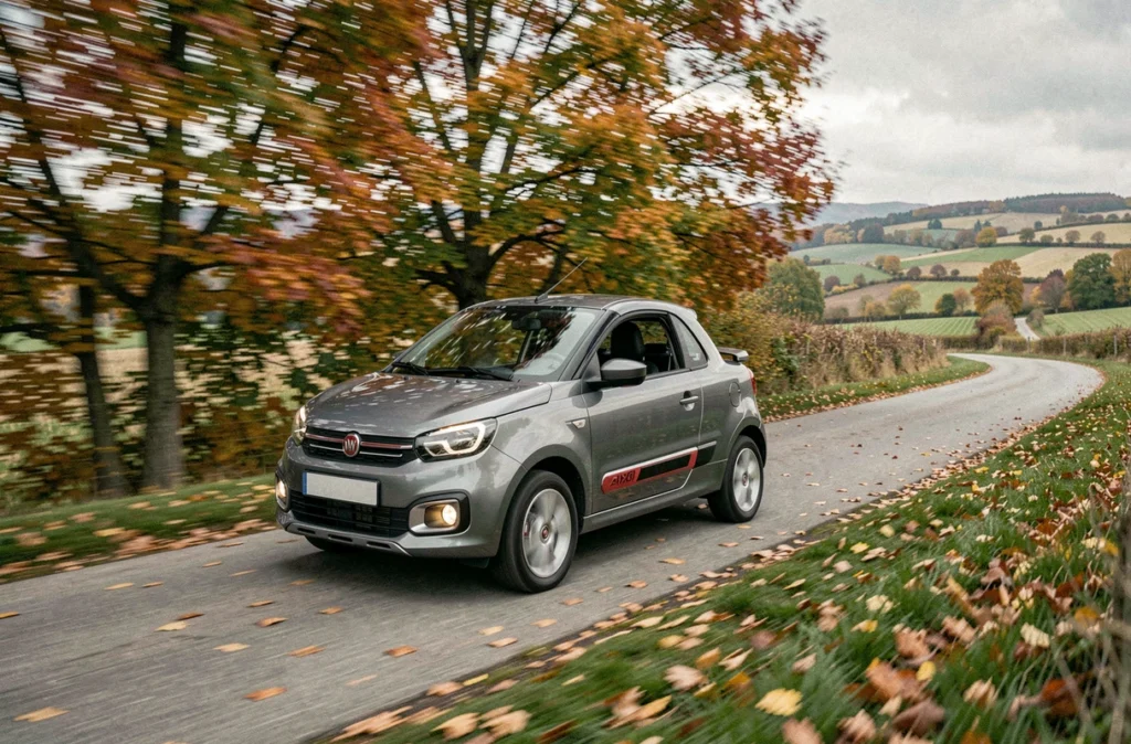 Aixam Coupé GTI gris métallisé en mouvement sur une route de campagne française entourée d'arbres aux couleurs automnales